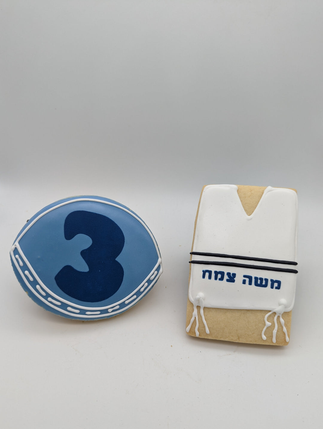 Blue cookie a with number 3 and another cookie resembling a prayer shawl on a white background